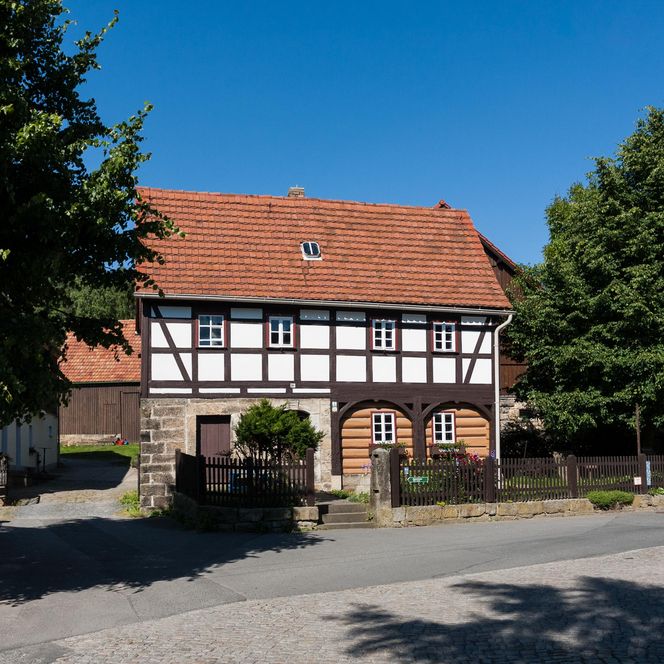 Fachwerkhaus mit roten Dächern und grünen Bäumen vor blauem Himmel.