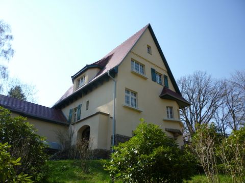 Großes Haus mit weißen Fensterrahmen, flankiert von üppigem grünen Garten und Bäumen.