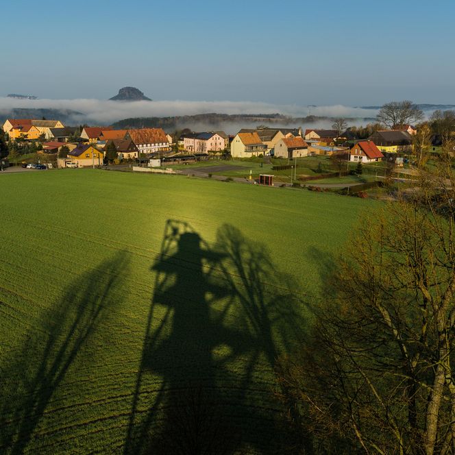 Grünes Feld mit Häusern im Hintergrund und einem klaren blauen Himmel.
