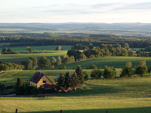 Grünes Tal mit Hügeln, bewaldeten Flächen und einem kleinen Dorf im Hintergrund.