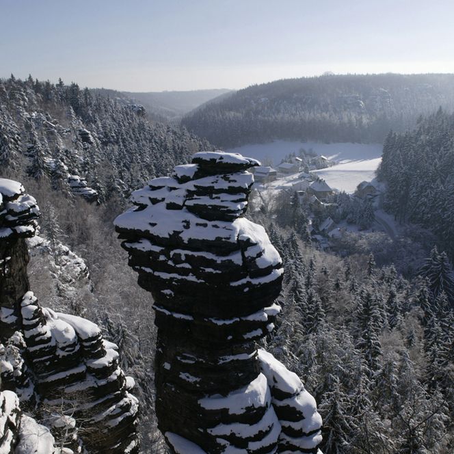 Schneebedeckte Felsen ragen über eine winterliche Landschaft mit einem Fluss und bewaldeten Hügeln.