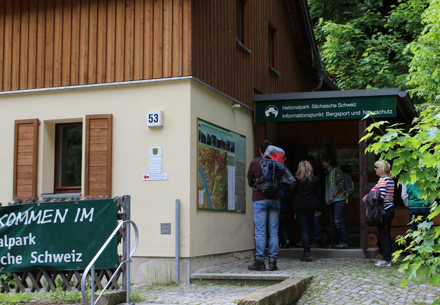 Eingang zur Infostelle Nationalpark in Schmilka mit Holzverkleidung, mehrere Personen stehen davor.