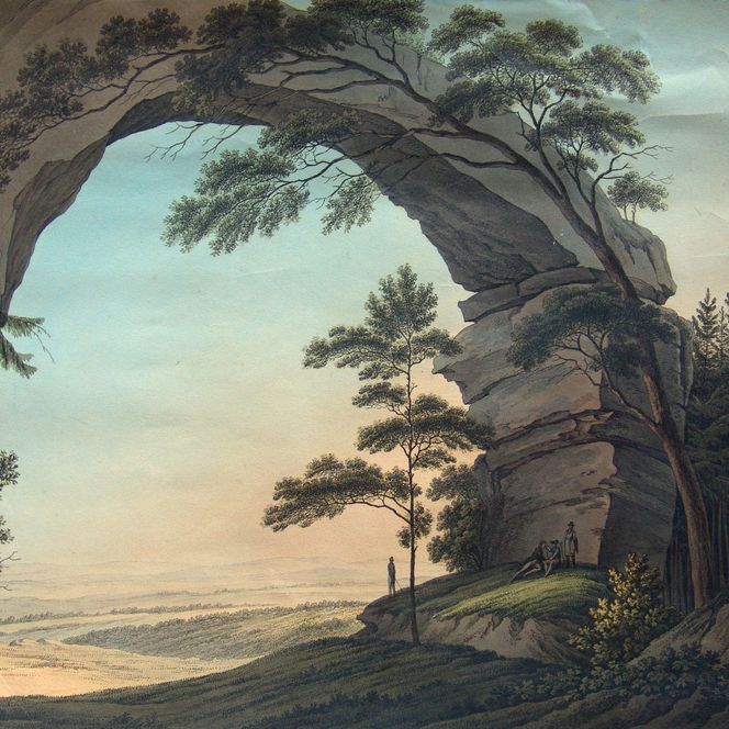 Blick durch einen großen Felsbogen auf eine Landschaft mit Bäumen und sanften Hügeln im Hintergrund.