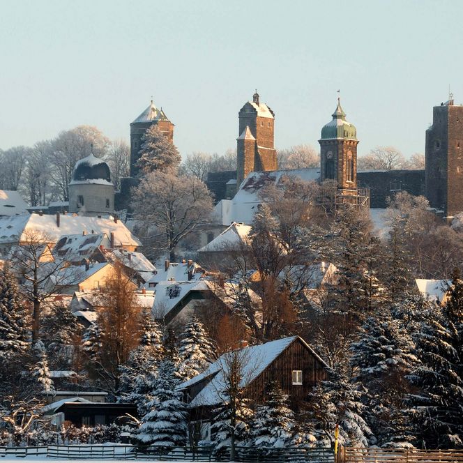 Schneebedeckte Landschaft mit einer Burg und historischen Gebäuden im Hintergrund.