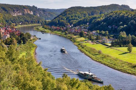 Blick auf einen Fluss, umgeben von grünen Hügeln und Bäumen, mit Booten auf dem Wasser.