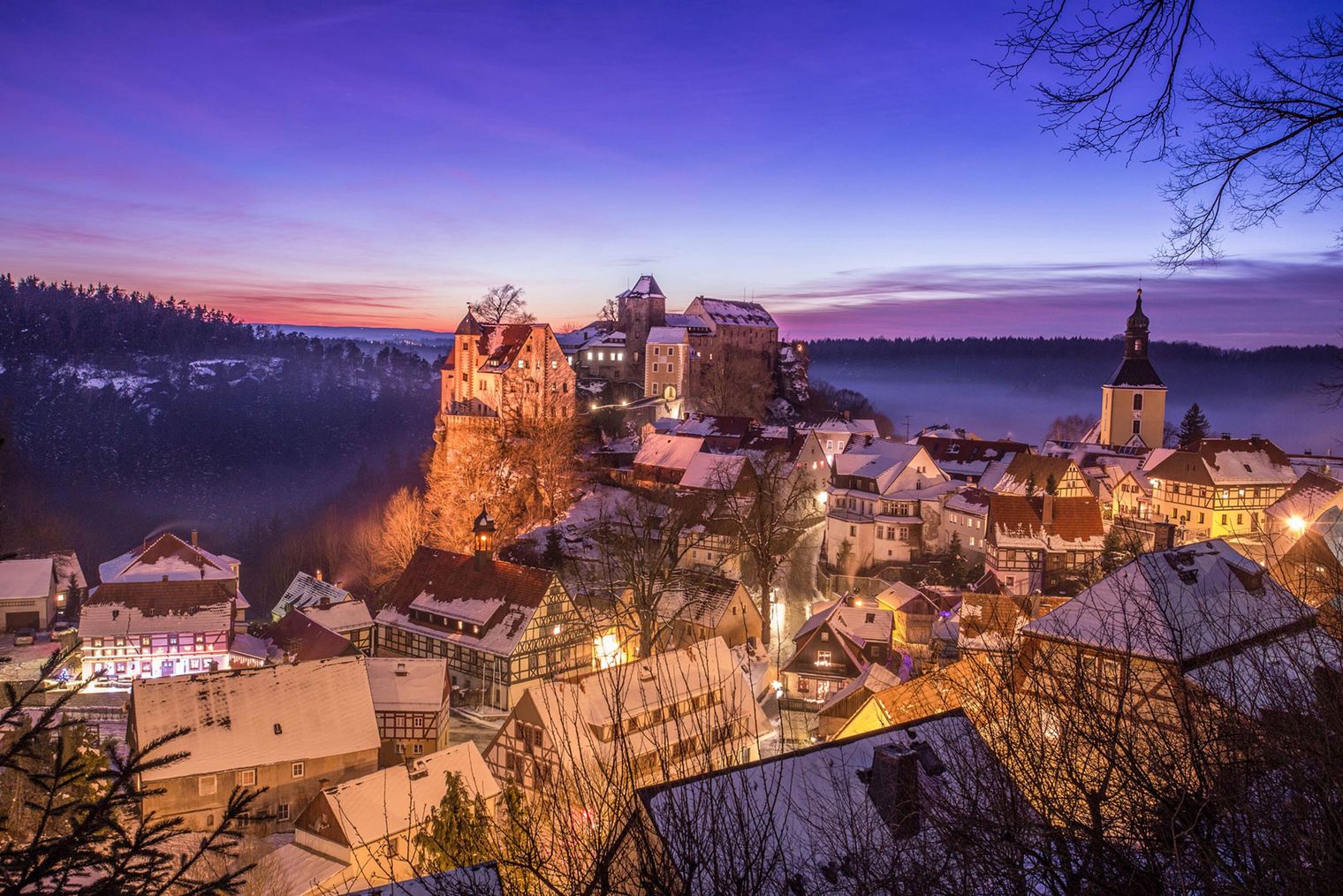 Blick auf eine malerische Stadt mit historischen Gebäuden und einer Burg bei Sonnenuntergang.