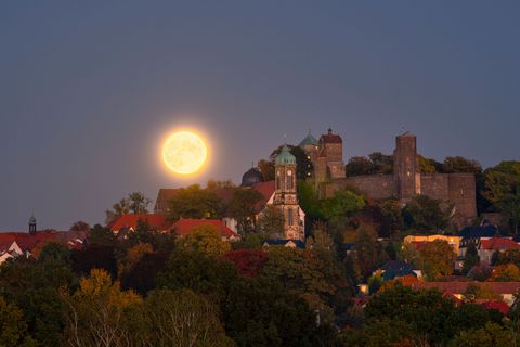 Vollmond über einer Stadt mit historischen Gebäuden und einer Burg im Hintergrund.