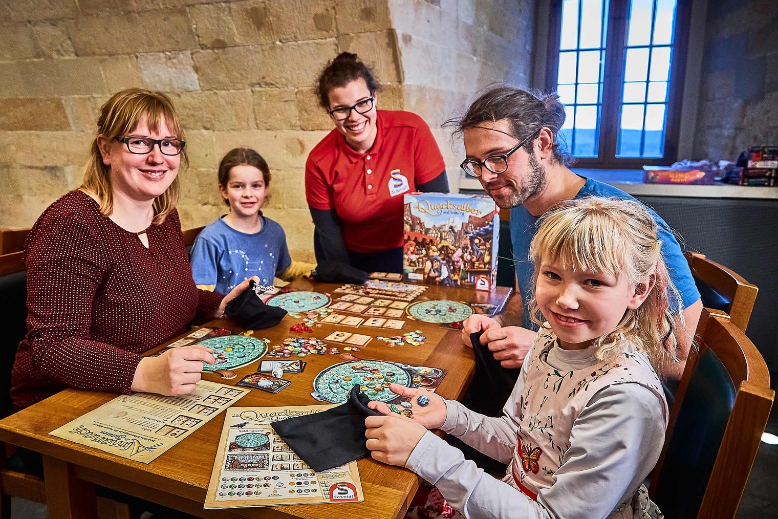 Familie spielt gemeinsam an einem Tisch mit einem Brettspiel in einem gemütlichen Raum.