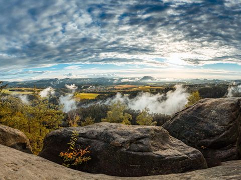 Panoramablick von Felsformationen und Wälder unter einem bewölkten, blauen Himmel.