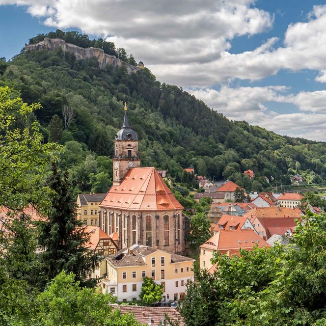 Blick auf eine Stadt mit bunten Häusern und einer Kirche, umgeben von grünen Hügeln und Wolken.