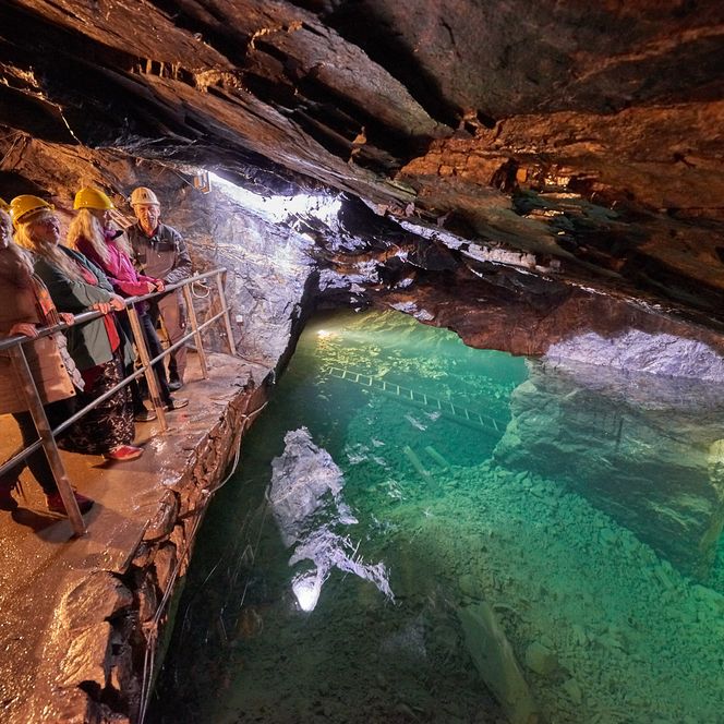 Besucher stehen an einem glitzernden Wasserbecken in einer Höhle mit reflektierendem Licht.
