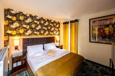 Modernes Hotelzimmer mit Doppelbett, dekorativer Wand, Nachttisch und Kunstwerk an der Wand.