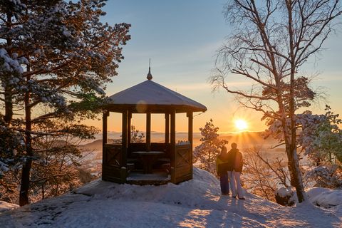 Winterlandschaft mit einem Pavillon und zwei Personen, die den Sonnenuntergang beobachten.