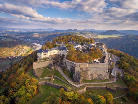Festung Königstein von oben mit bewaldeten Hügeln, bewölktem Himmel und herbstlichen Bäumen.
