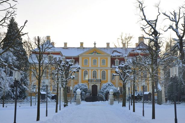 Barockschloss Rammenau im Winter, verschneit, blauer Himmel, Garten im Vordergrund.