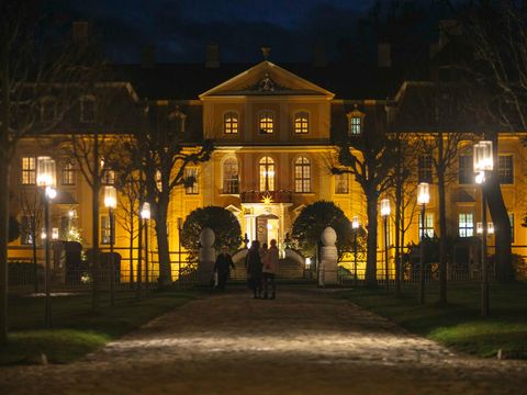Barockschloss Rammenau bei Nacht im Winter, beleuchtet, mit verschneiten Bäumen.