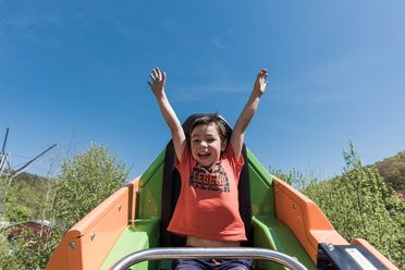 Ein Kind mit erhobenen Händen sitzt in einer Achterbahn und lächelt vor Freude.