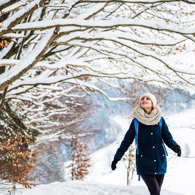 Person mit Mütze fotografiert einen Sonnenuntergang über einer winterlichen Landschaft.