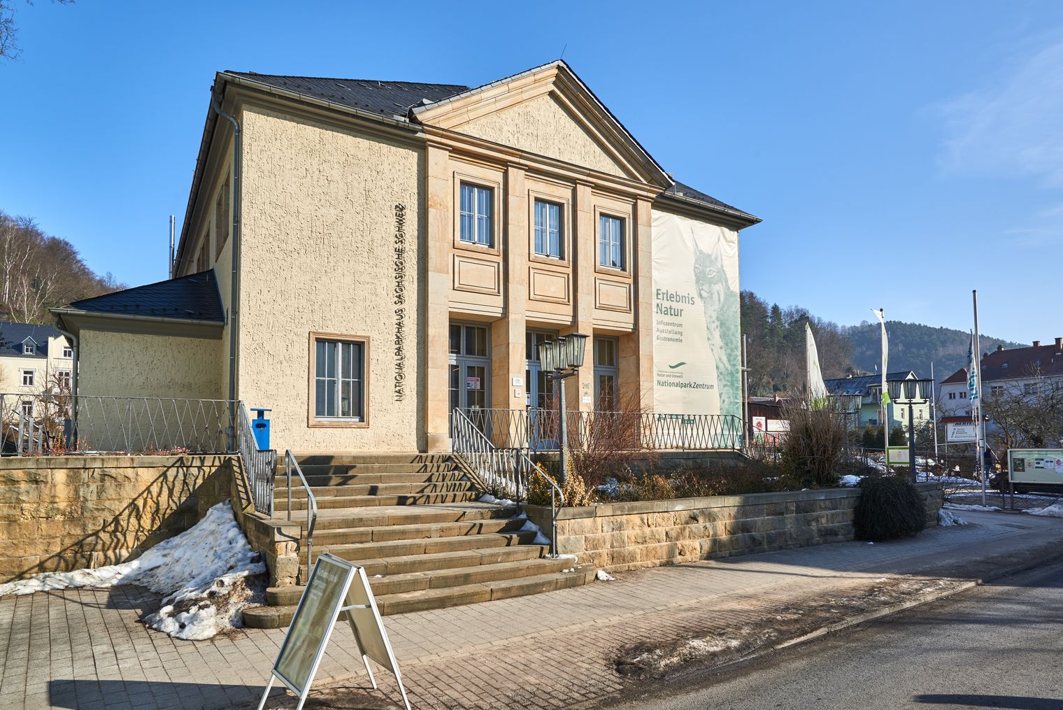 Außenansicht des NationalparkZentrum mit Säulen, Treppe und Fenstern, umgeben von einer Straße und Bäumen.