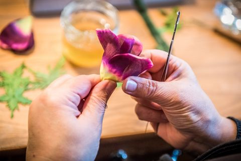 Hände halten lila Seidenblumen-Blätter, während eine Nadel in der anderen Hand gehalten wird.
