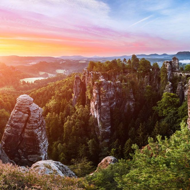 Sonnenuntergang über einem dicht bewaldeten und felsigem Gebiet mit farbenfrohem Himmel.