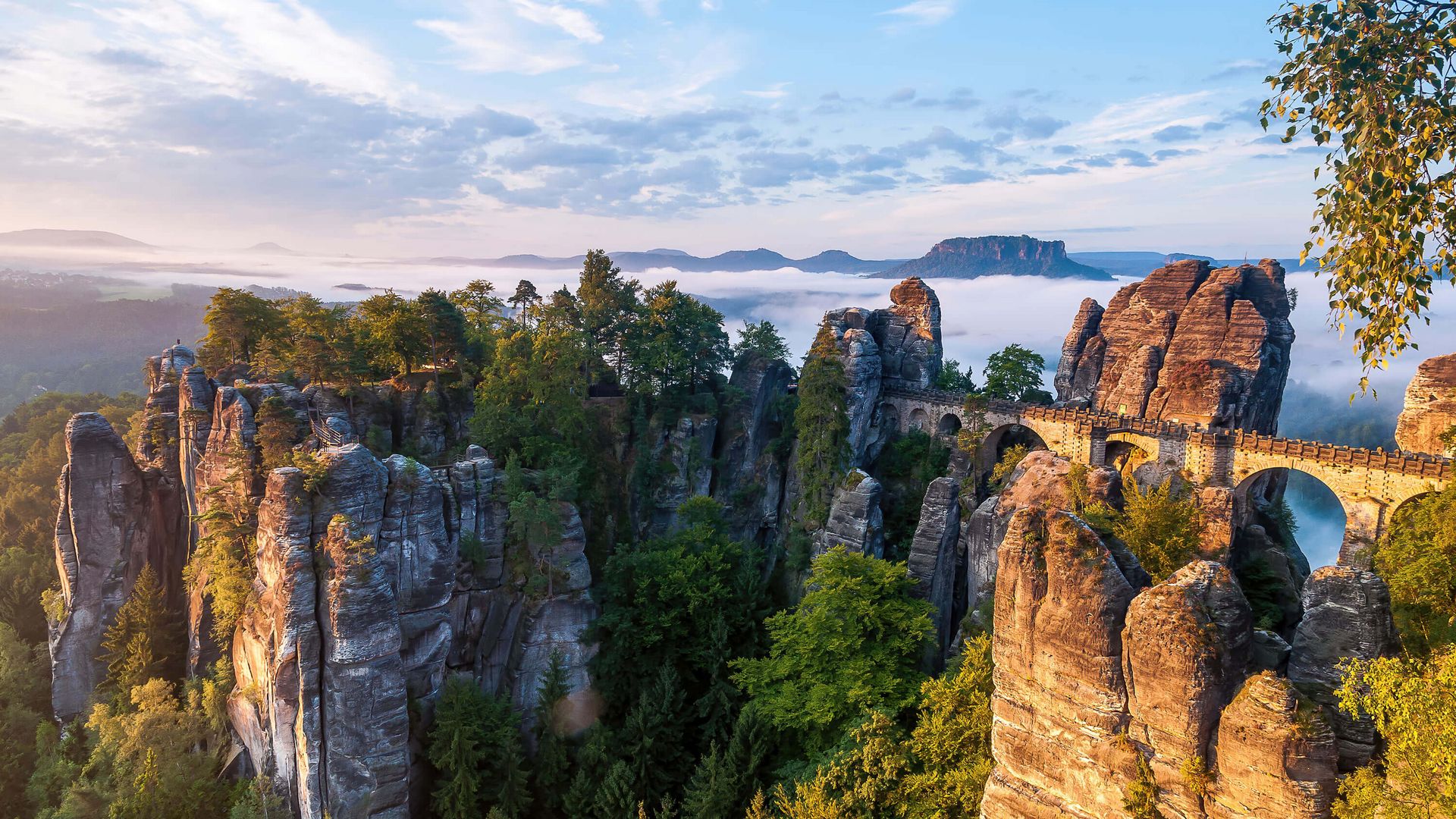Felsenlandschaft mit grünen Bäumen und Wolken im Hintergrund, bei Sonnenaufgang.