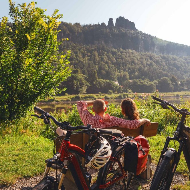 Vier Personen posieren mit Fahrrädern in einer grünen Landschaft, im Hintergrund Berge und Bäume.