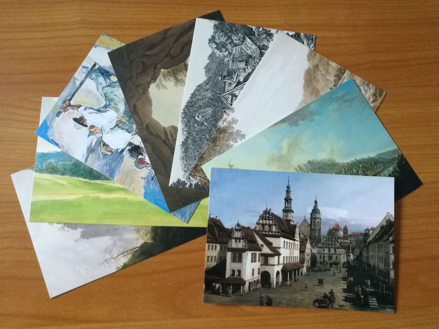Mehrere Postkarten mit Landschafts- und Stadtansichten auf einem Holztisch.