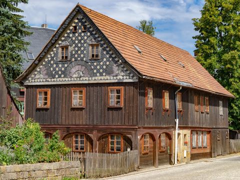  Umgebindehaus in Hinterhermsdorf mit braunem Holz, umgeben von grünen Bäumen.