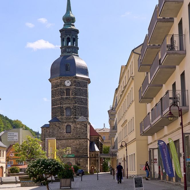 Kirche mit Turm und Turmuhr, umgeben von modernen und alten Gebäuden.