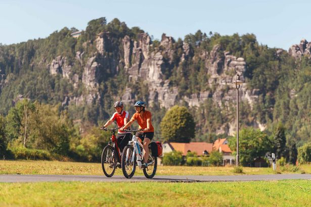 Elberadweg bei Kurort Rathen: Radfahrer auf einem Waldweg, umgeben von hohen Felsen in der Sächsischen Schweiz.