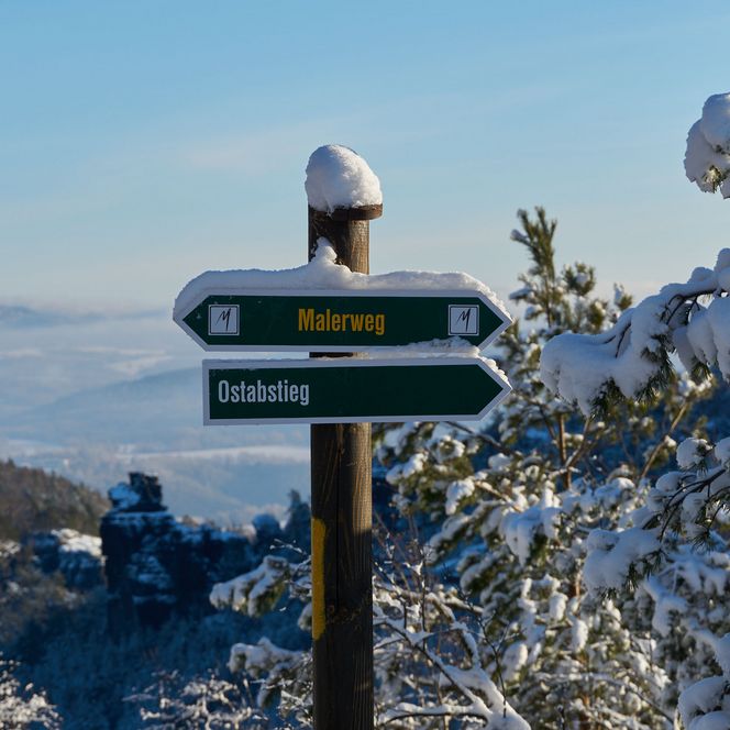 Wegweiser mit Richtungshinweisen im verschneiten Landschaftsbild.