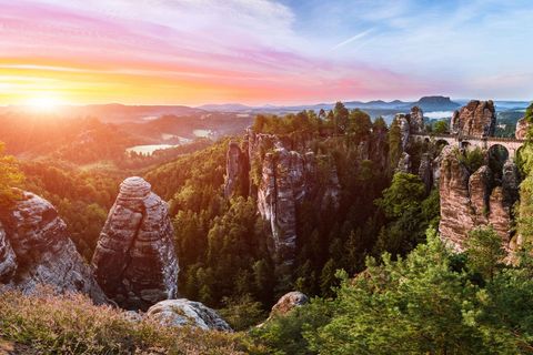 Sonnenaufgang über einer felsigen Landschaft mit Bäumen und einem weiten Blick auf das Tal.