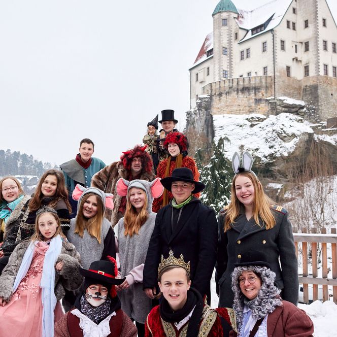 Gruppe von Menschen in historischen Kostümen vor einem Schloss im Schnee.