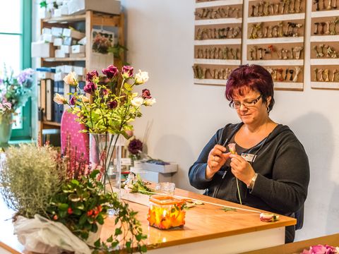 Frau sitzt an Tisch und stellt Kunstblumen her.