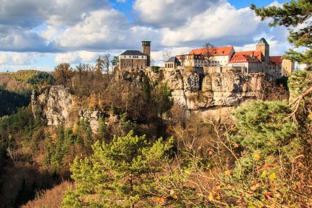 Burg auf einem Felsen, umgeben von Bäumen und bewaldeten Hügeln unter einem bewölkten Himmel.
