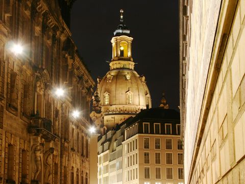Beleuchtete Dresdner Skyline mit Frauenkirche, Fürstenzug und reflektierenden Lichtern bei Nacht.