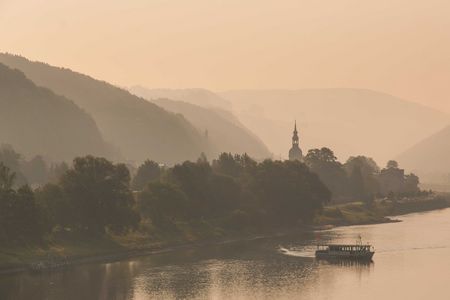 Sanfte Hügel und Bäume am Fluss, im Hintergrund eine Silhouette eines Turms in der Dämmerung.