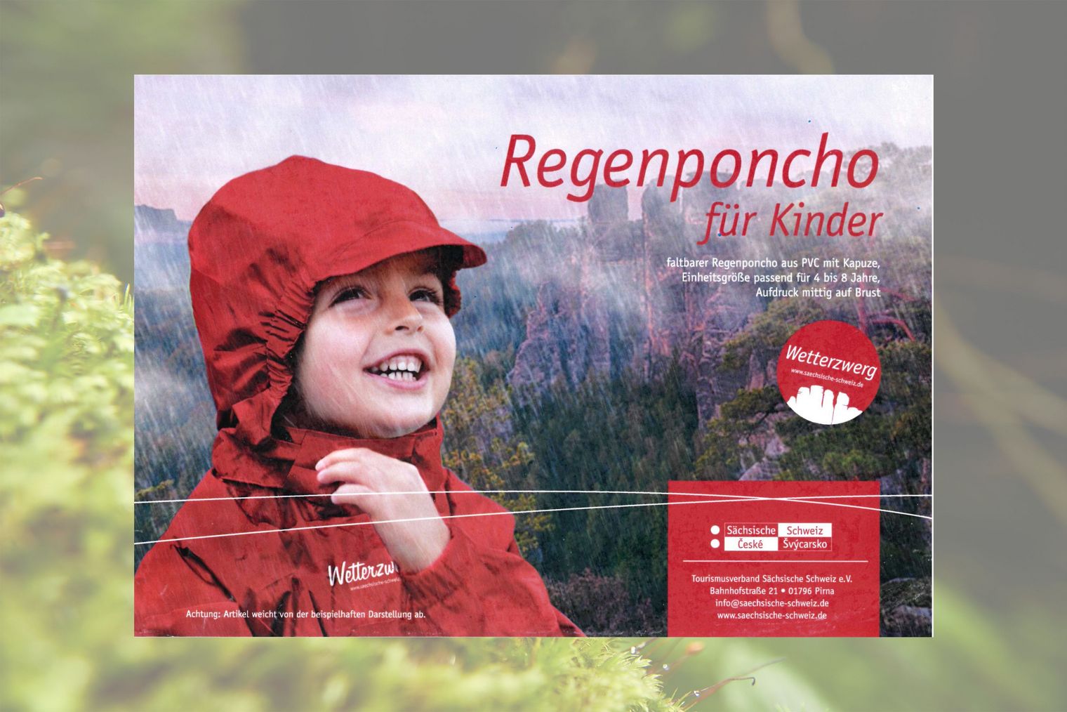 Kind in rotem Regenponcho mit Kapuze, lächelt vor einer regnerischen Landschaft.