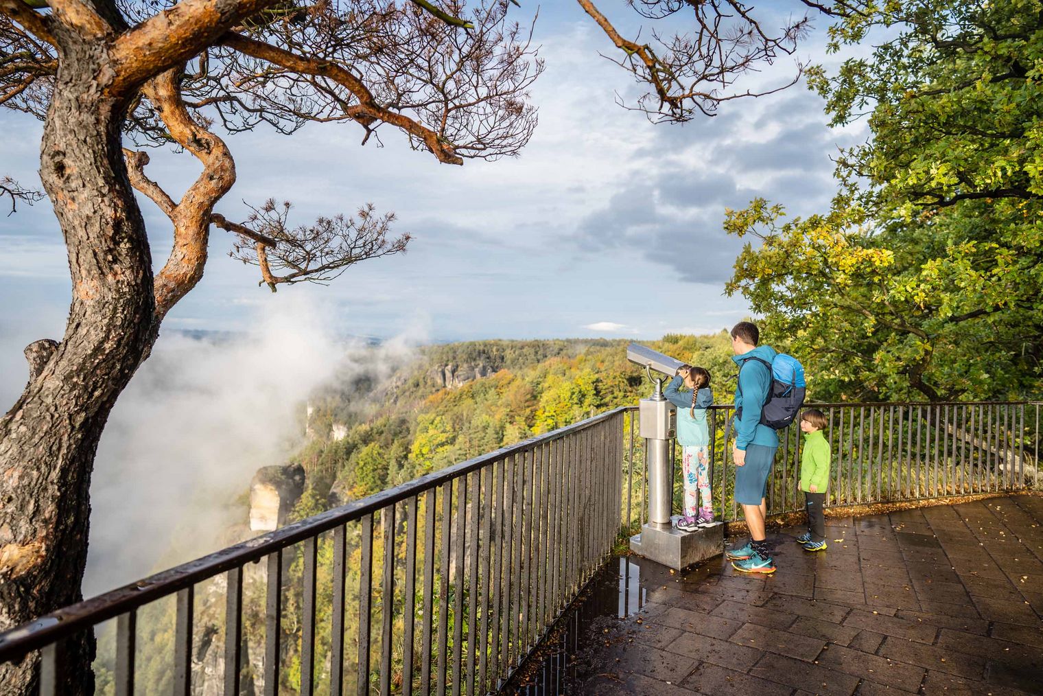 Mann und Kind stehen an einem Aussichtspunkt mit Blick auf eine Landschaft und dampfende Felsen.