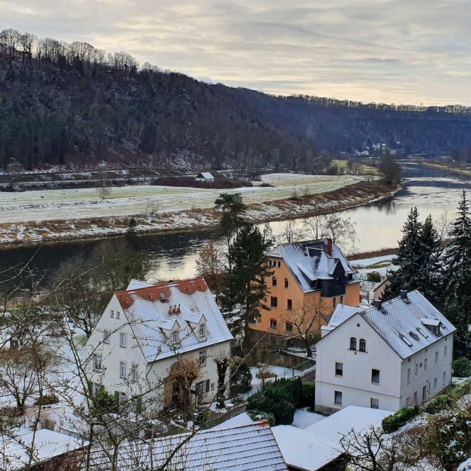 Blick auf ein Tal mit einem Fluss, umgeben von Hügeln und schneebedeckten Häusern.