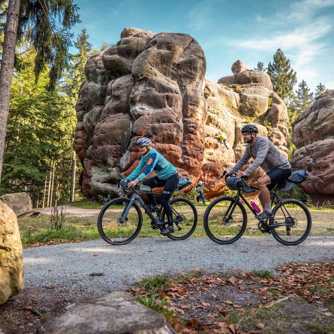 Zwei Radfahrer fahren auf einem Weg zwischen den Felsformationen der Oberlausitzer Kelchsteine im Wald.