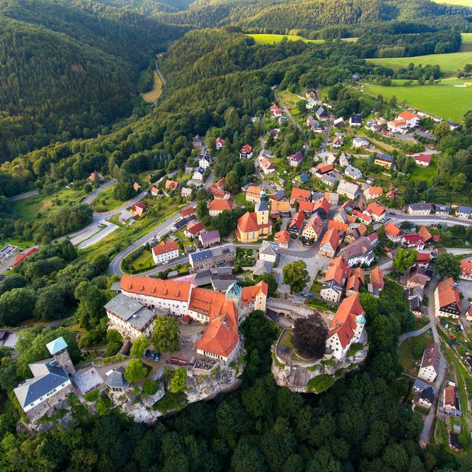 Luftaufnahme eines kleinen Dorfes mit roten Dächern, umgeben von grünen Wäldern und Feldern.