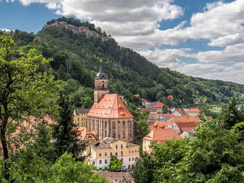 Panorama der Stadt Königstein mit Festung auf einem Hügel, umgeben von grünen Wäldern.