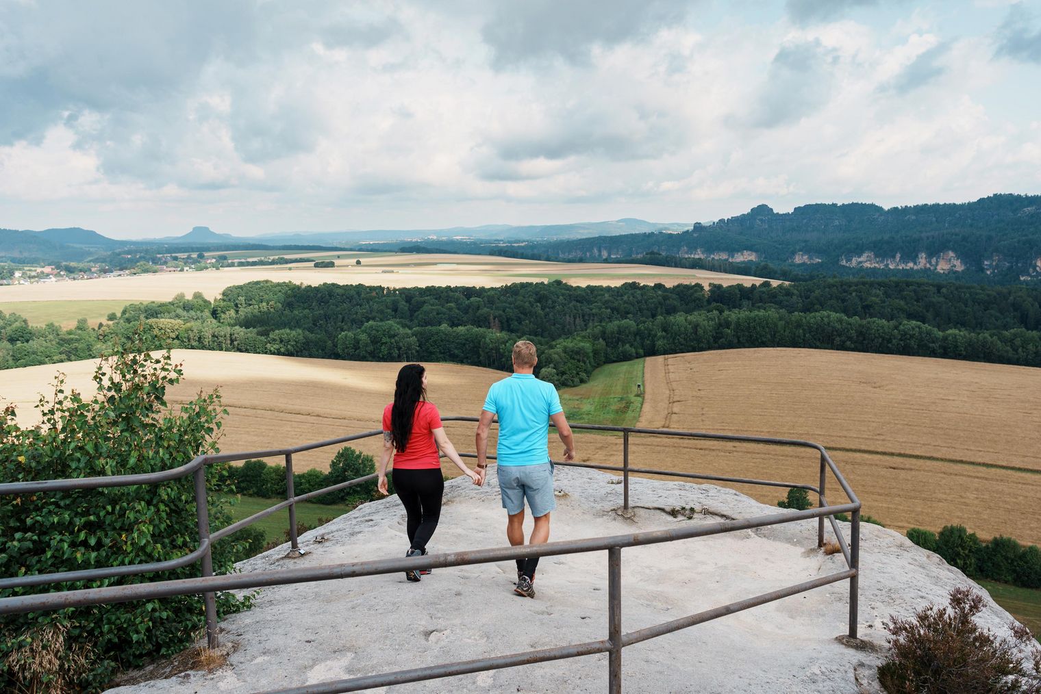 Paar hält Händchen und geht eine Treppe hinunter mit Blick auf eine weite Landschaft.