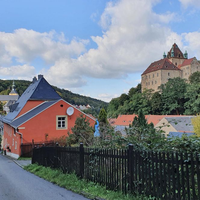 Bunte Häuser und eine Burg auf einem Hügel unter einem blauen Himmel mit Wolken.