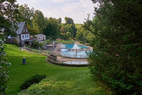 Grüne Wiese mit einem Pool und einem Pavillon, umgeben von Bäumen und einem Haus im Hintergrund.