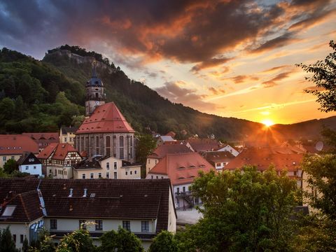 Sonnenuntergang über Festung Königstein, Kirche und Häuser im Vordergrund, orange-rosa Himmel.