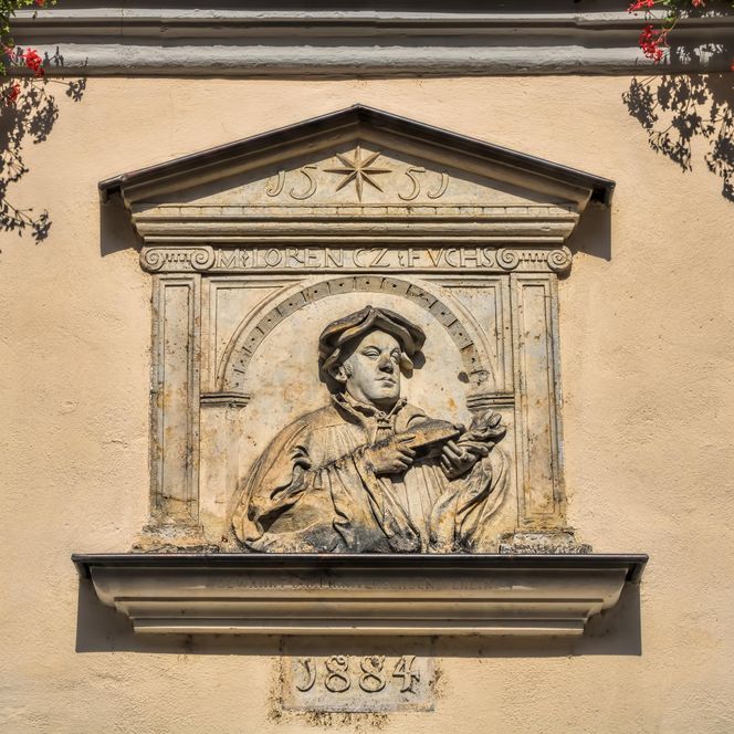 Relief einer Figur mit Krone und Zepter, umgeben von Blumen.