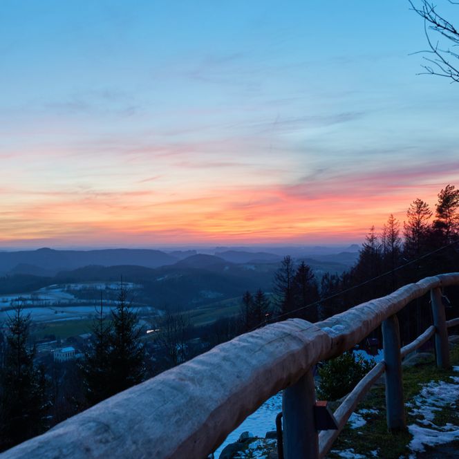 Blick auf eine winterliche Landschaft mit schneebedeckten Bäumen und einem bunten Sonnenuntergang.